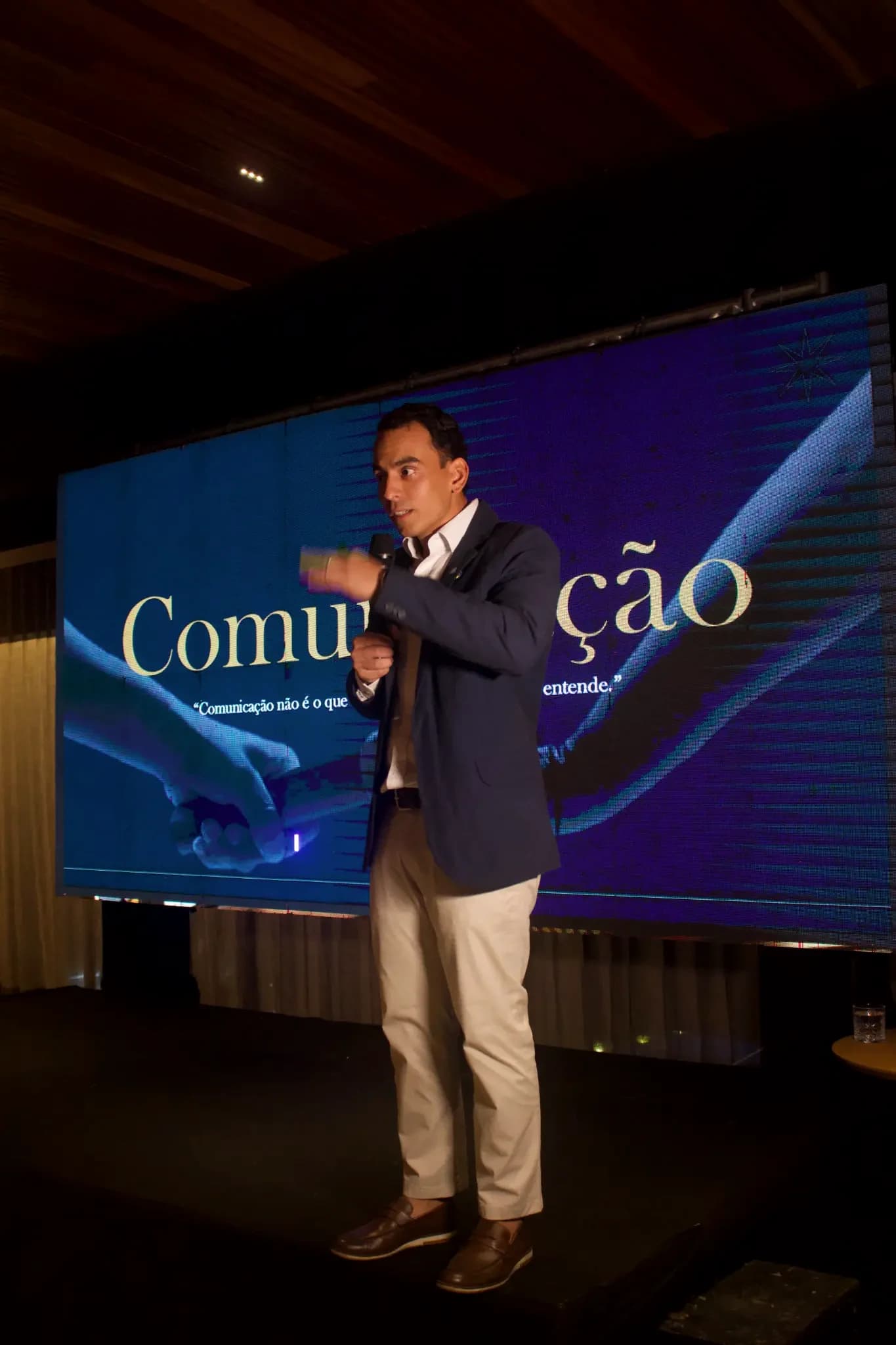 Vitor Novaes no palco, de blazer, durante a palestra