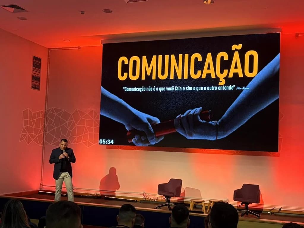 Vitor Novaes no palco, com o telão sobre comunicação ao fundo